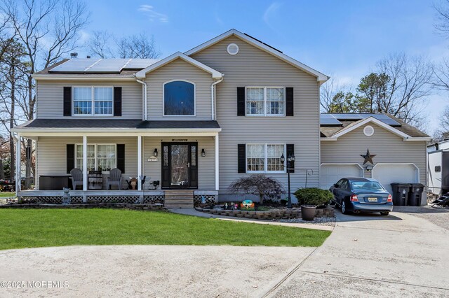 view of front of house featuring roof mounted solar panels, covered porch, a front lawn, an attached garage, and driveway