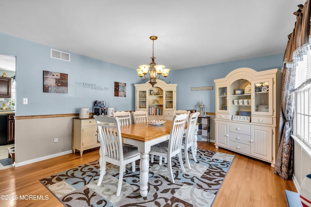 dining room featuring light wood-style floors, a notable chandelier, baseboards, and visible vents