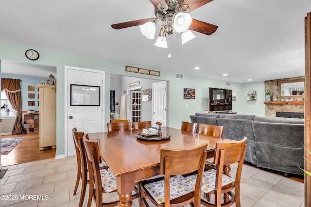 dining space with ceiling fan, a stone fireplace, visible vents, recessed lighting, and baseboards