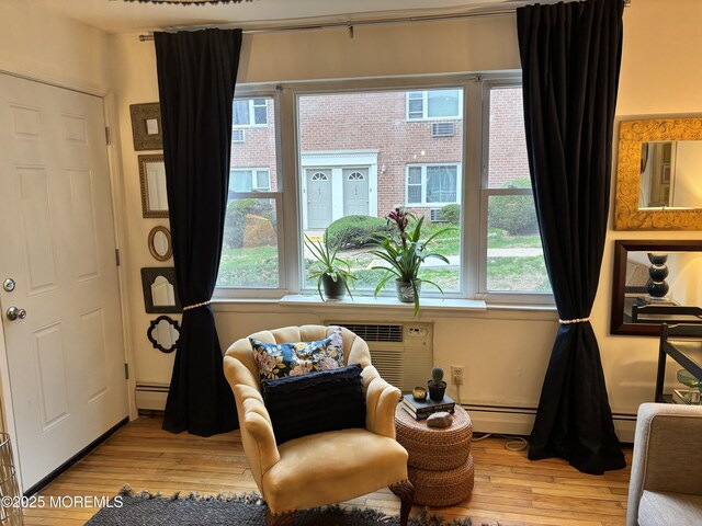 living area with baseboard heating, wood finished floors, an AC wall unit, and a wealth of natural light
