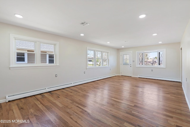 unfurnished living room with baseboard heating, a healthy amount of sunlight, and wood finished floors
