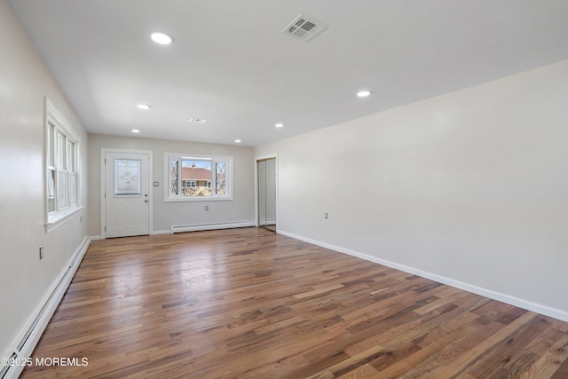 empty room featuring visible vents, a baseboard heating unit, and wood finished floors
