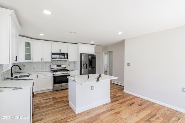 kitchen with a baseboard heating unit, a center island, light wood-style floors, decorative backsplash, and stainless steel appliances