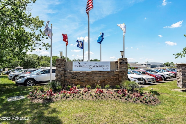 community / neighborhood sign featuring uncovered parking and a lawn