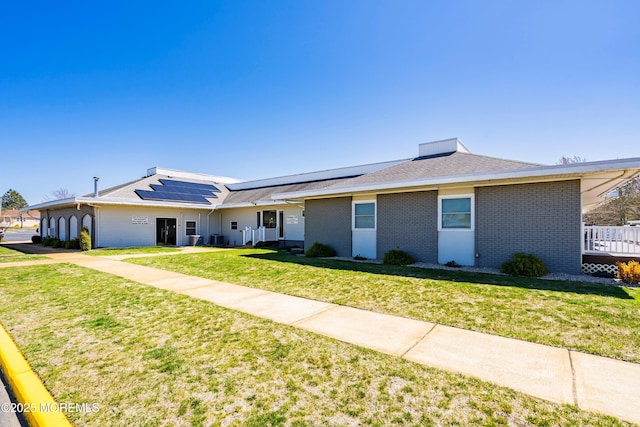 ranch-style home with a front yard, brick siding, and solar panels