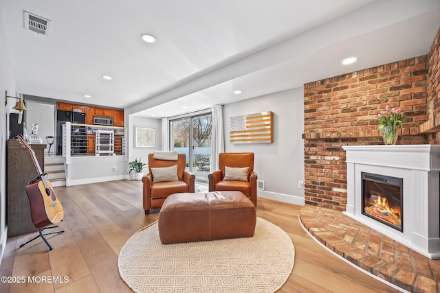 living room featuring light wood-style flooring, visible vents, a glass covered fireplace, baseboards, and recessed lighting