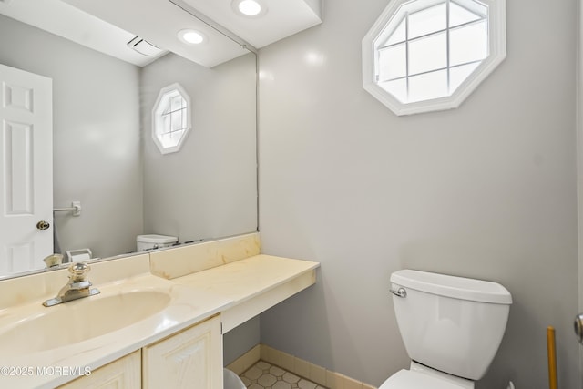 half bath with toilet, vanity, baseboards, and visible vents