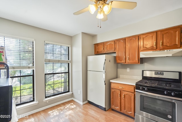 kitchen featuring freestanding refrigerator, under cabinet range hood, gas stove, light countertops, and plenty of natural light