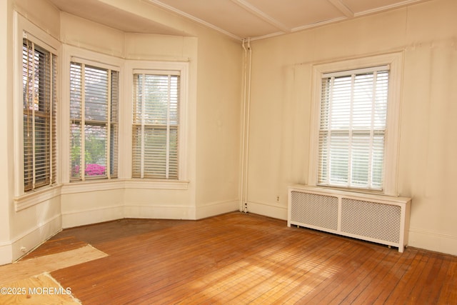 unfurnished room featuring baseboards, radiator, and hardwood / wood-style flooring