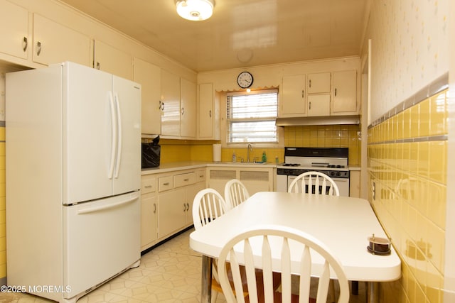 kitchen featuring white appliances, light countertops, under cabinet range hood, white cabinets, and a sink
