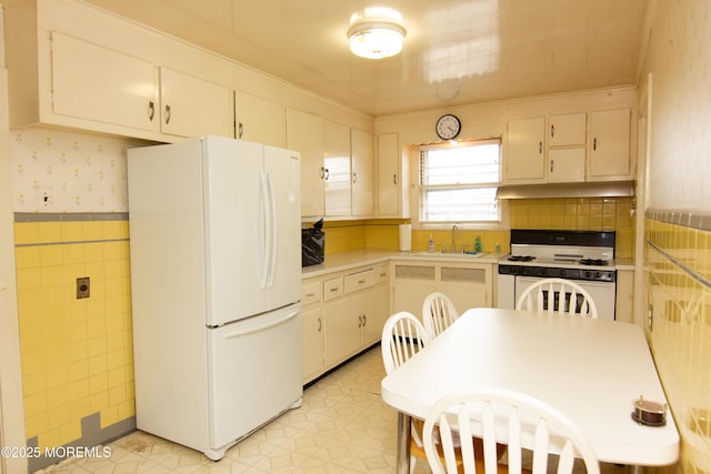kitchen featuring a sink, white appliances, light countertops, wallpapered walls, and under cabinet range hood
