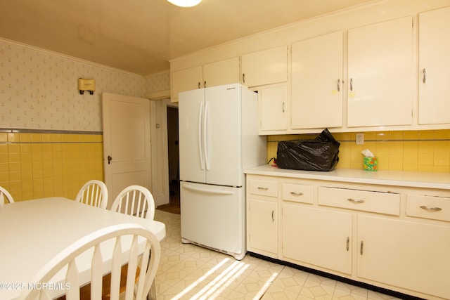 kitchen with freestanding refrigerator, white cabinetry, light countertops, wainscoting, and wallpapered walls