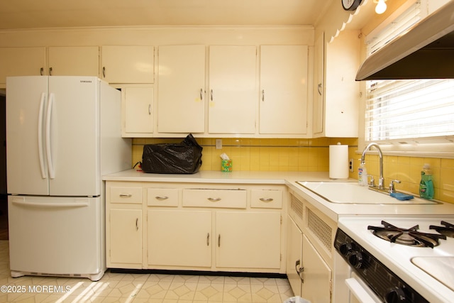 kitchen featuring light countertops, under cabinet range hood, white appliances, and a sink