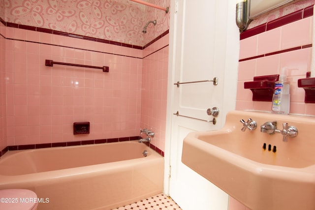 bathroom featuring toilet,  shower combination, wallpapered walls, and a sink