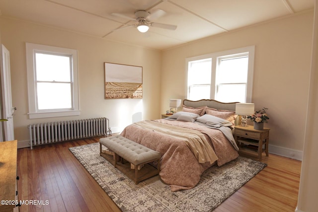 bedroom with radiator heating unit, baseboards, multiple windows, and hardwood / wood-style flooring