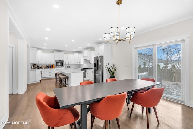dining area with light wood-style floors, a chandelier, and ornamental molding