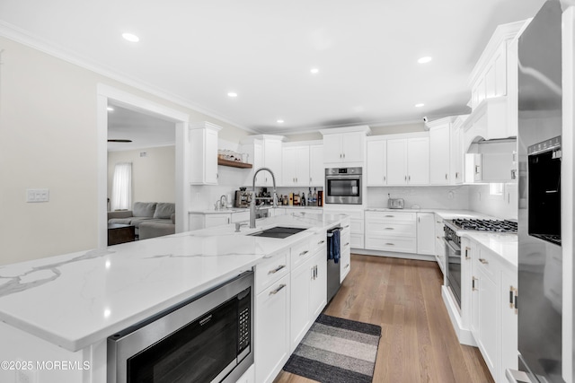 kitchen with a sink, stainless steel appliances, light wood finished floors, white cabinets, and ornamental molding