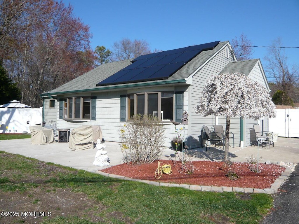 bungalow-style house with a patio, a shingled roof, and roof mounted solar panels