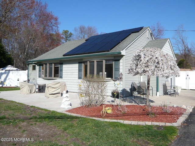 bungalow-style house with a patio, a shingled roof, and roof mounted solar panels