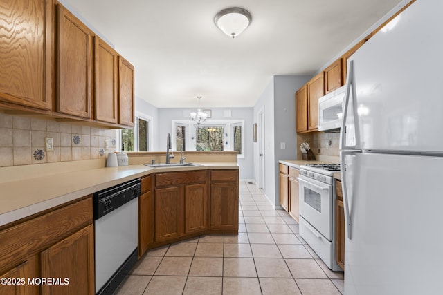 kitchen with brown cabinets, a sink, white appliances, decorative backsplash, and a chandelier