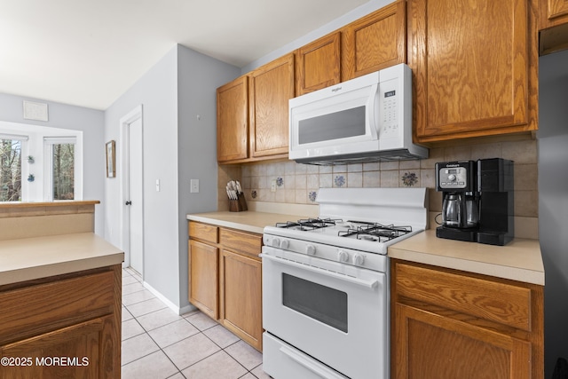 kitchen featuring backsplash, white appliances, brown cabinetry, light countertops, and light tile patterned floors