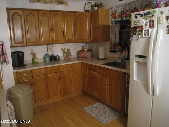 kitchen with brown cabinetry, light wood-style floors, a sink, and white fridge with ice dispenser