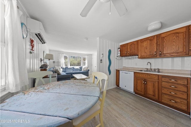 kitchen with brown cabinetry, white dishwasher, a sink, and a wall unit AC
