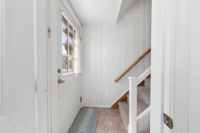 doorway featuring a decorative wall, baseboards, stone finish flooring, and stairway