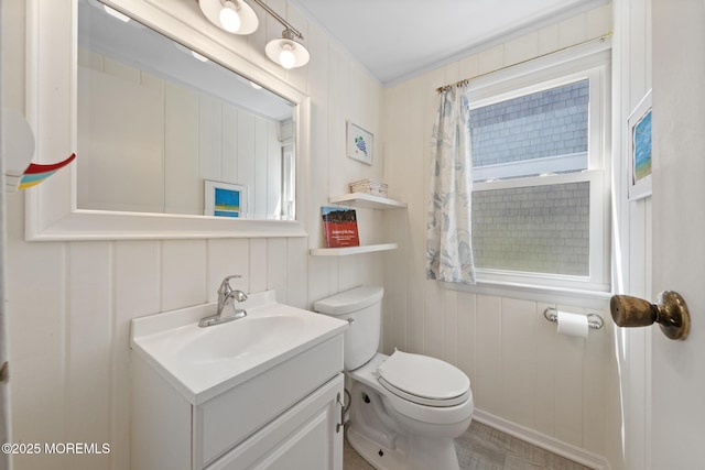 bathroom with toilet, a decorative wall, and vanity
