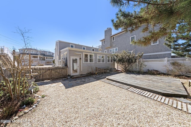 rear view of property with a deck, a chimney, and fence