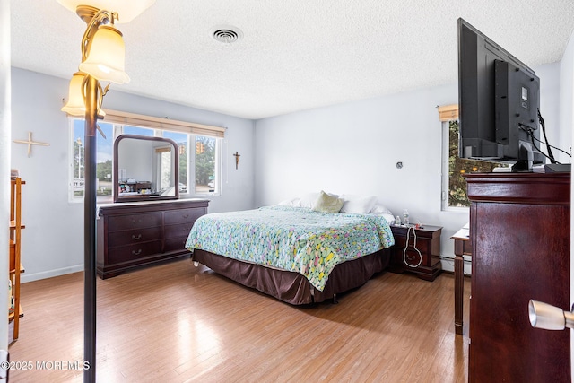 bedroom featuring baseboard heating, a textured ceiling, baseboards, wood finished floors, and visible vents