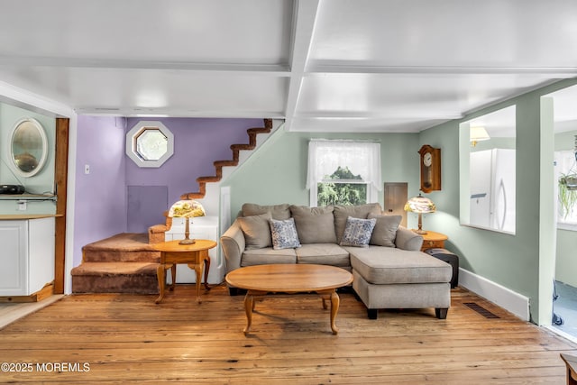 living area featuring light wood-type flooring, visible vents, stairway, and beamed ceiling