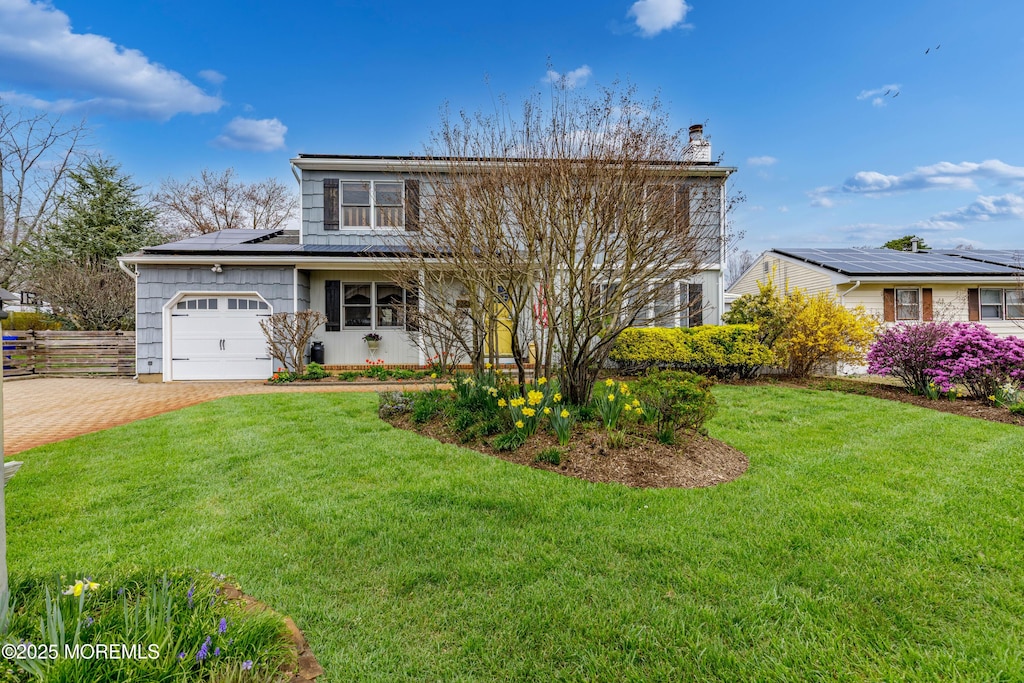 traditional-style home with roof mounted solar panels, decorative driveway, a front yard, a chimney, and a garage