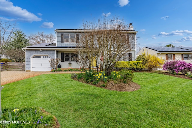 traditional-style home with roof mounted solar panels, decorative driveway, a front yard, a chimney, and a garage