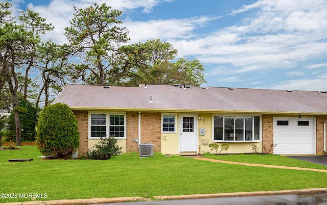 view of front of property featuring central air condition unit, a front lawn, aphalt driveway, a garage, and brick siding