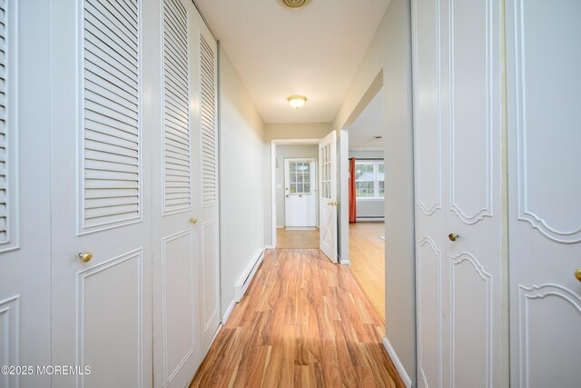 hallway featuring a baseboard heating unit, baseboards, and light wood-style floors