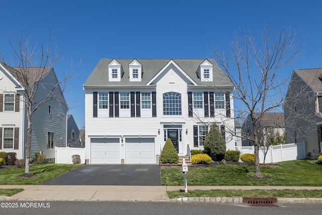 colonial inspired home with an attached garage, a front lawn, fence, and driveway