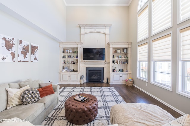 living area with a towering ceiling, dark wood finished floors, baseboards, a glass covered fireplace, and ornamental molding