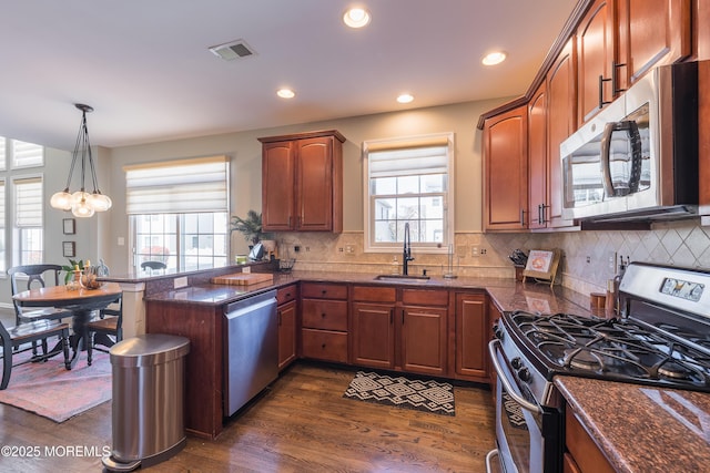 kitchen featuring visible vents, dark wood-style flooring, a peninsula, a sink, and stainless steel appliances