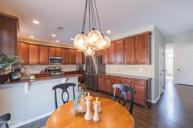 kitchen featuring tasteful backsplash, stainless steel appliances, a peninsula, a kitchen bar, and visible vents