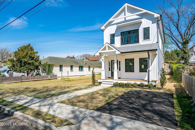 view of front of home with covered porch, fence, board and batten siding, and a front yard
