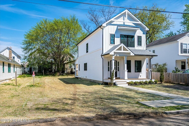 view of front of home with covered porch, fence, board and batten siding, and a front lawn