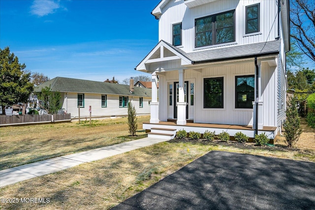 modern farmhouse with a porch, fence, board and batten siding, and a front lawn