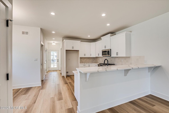 kitchen with a kitchen breakfast bar, stainless steel microwave, a peninsula, light wood-style floors, and white cabinetry