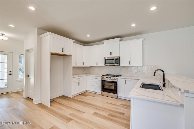 kitchen featuring a peninsula, light wood-type flooring, light stone counters, a sink, and stainless steel appliances