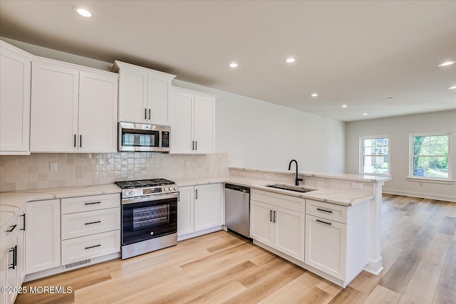 kitchen featuring a peninsula, recessed lighting, white cabinets, a sink, and stainless steel appliances