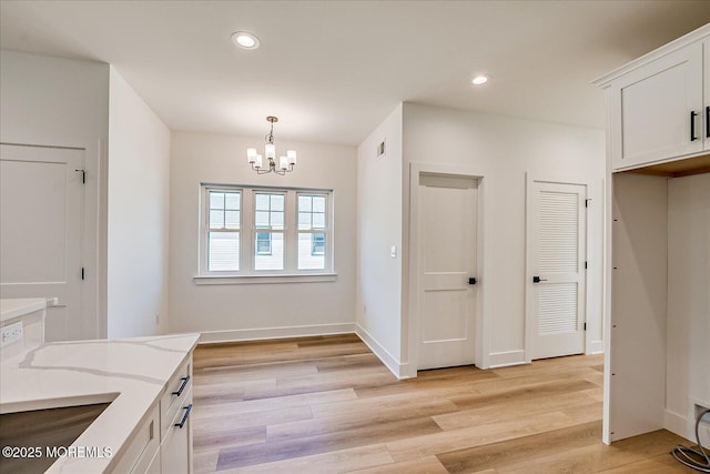 kitchen featuring light wood-type flooring, white cabinetry, a chandelier, and light stone countertops