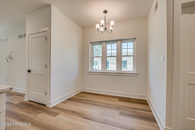 unfurnished dining area featuring visible vents, light wood finished floors, baseboards, and a notable chandelier