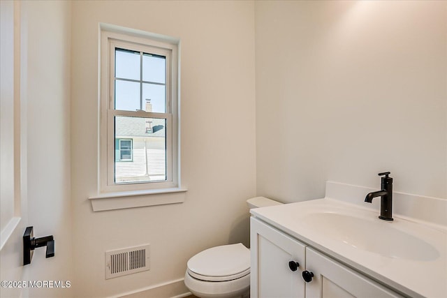half bath featuring vanity, baseboards, toilet, and visible vents