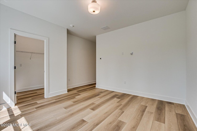 unfurnished bedroom featuring a walk in closet, baseboards, a closet, and light wood-style flooring